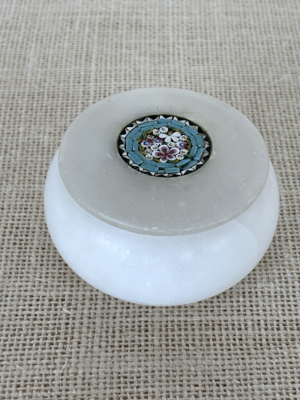 A round white alabaster jar with a matching lid featuring a colorful floral micro mosaic tile in the center