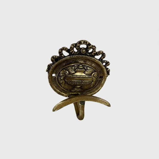 A baroque style brass coat hook with a center back urn motf and top bow detail.